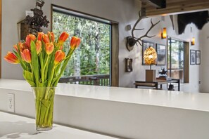 A vase with tulips on a white countertop, a window with a view of trees, and a wall-mounted deer head decoration. - Mule Deer - Grand Mt. Hood Chalet for Groups (Government Camp)