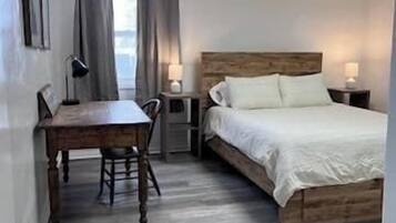 Une chambre à coucher avec un lit en bois, un bureau, une chaise, une table de chevet et une fenêtre avec des rideaux.