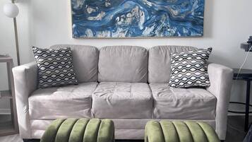 Un salon moderne avec un canapé gris, des coussins à motifs et des poufs verts.