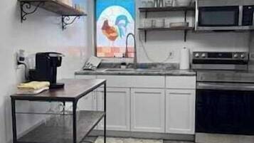 Une cuisine avec des armoires blanches, un four à micro-ondes, un four, une machine à café et une étagère sur laquelle est accrochée une pancarte indiquant « Cuisine ».