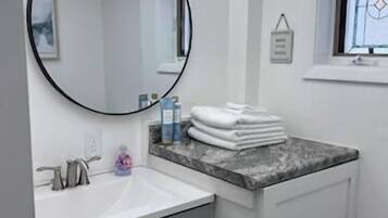 Une salle de bain avec un miroir rond, un lavabo, une fenêtre et un porte-serviettes.