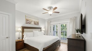 A bedroom with a bed, nightstands, a ceiling fan, a TV, and a view of greenery outside. - New! Epic Reunion Retreat (Kissimmee)