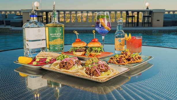 A table with food and drinks by a poolside, including bottles of liquor and a glass of cocktail. - New! Epic Reunion Retreat (Kissimmee)