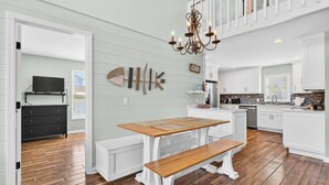 Een moderne keuken met witte kasten, een houten eettafel met banken en een kroonluchter.