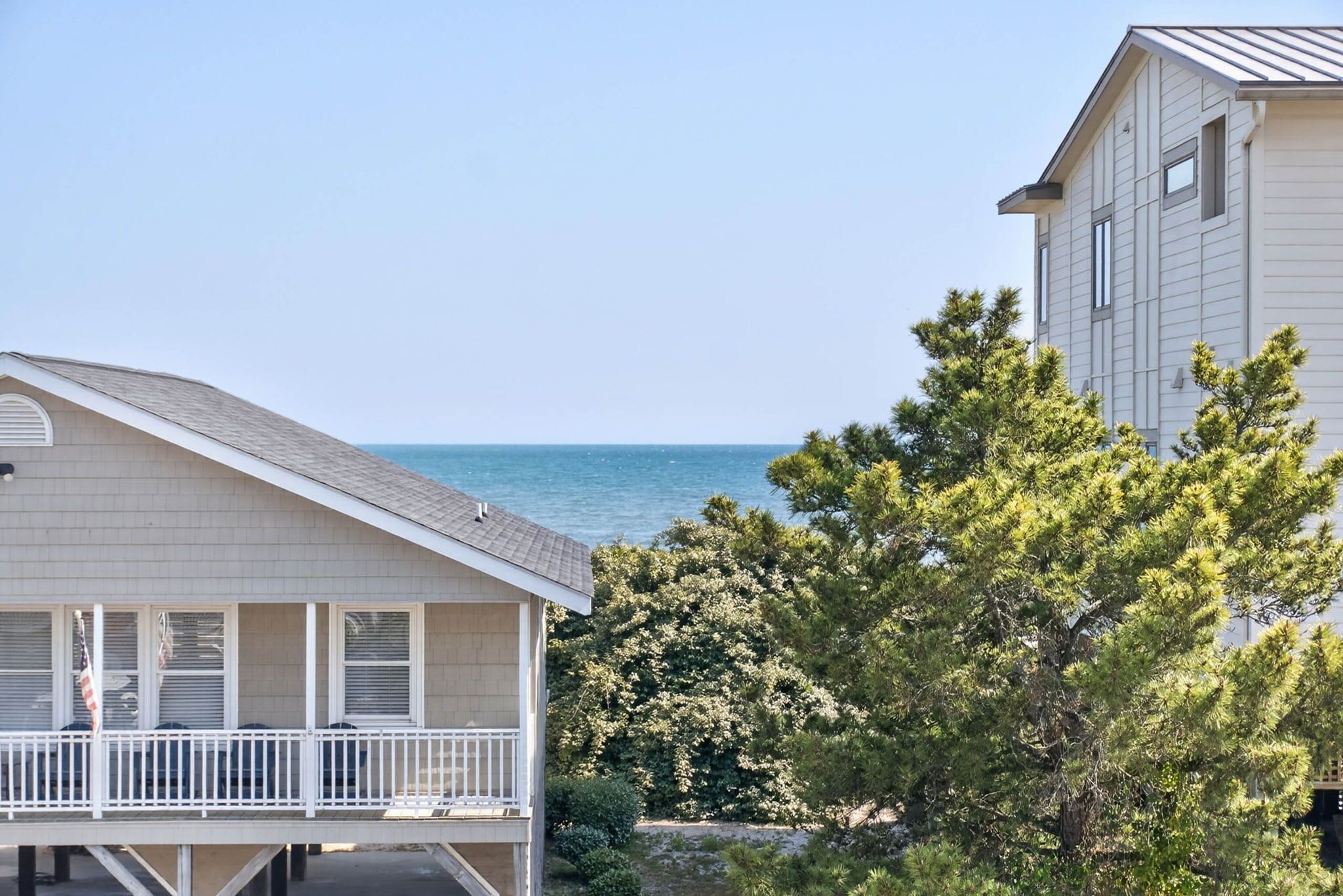 A coastal house with a balcony, a view of the sea, and a large tree in the foreground.