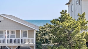 Een huis aan de kust met een balkon, uitzicht op zee en een grote boom op de voorgrond.
