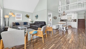 Een ruime woonkamer met een bank, stoelen, een eettafel en een keuken op de achtergrond.