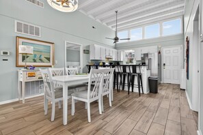 A spacious kitchen with white cabinetry, a dining area with white chairs, and a ceiling fan. - Crow's Nest by Brunswick Vacation Rentals: 4BR Pool Home Walk to Beach Sleeps 12 (Ocean Isle Beach)