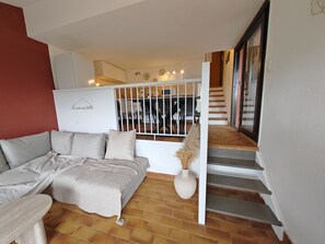 A living room with a sofa, a dining area with chairs and a table, and a staircase. - House Vetta di Sole air-conditioned sea view (Grosseto-Prugna)
