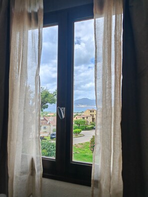 A window with curtains, a view of a residential area, and a distant mountain. - House Vetta di Sole air-conditioned sea view (Grosseto-Prugna)