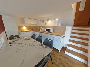 A compact kitchen with a marble countertop, white cabinets, a microwave, and a dining area with chairs and a table. - House Vetta di Sole air-conditioned sea view (Grosseto-Prugna)