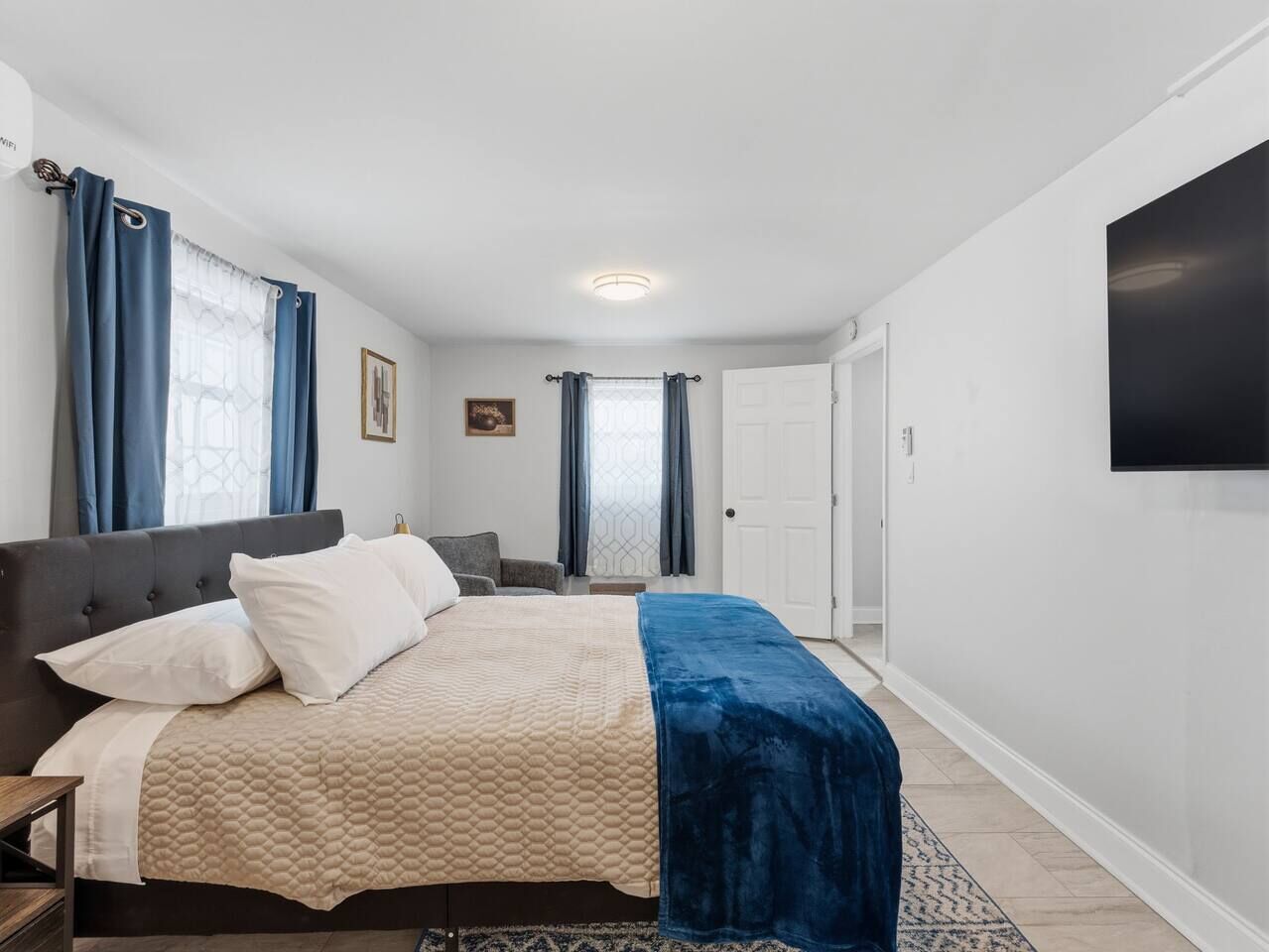 Un dormitorio con cama, una silla, un escritorio y un televisor en la pared.