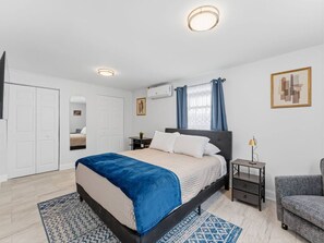 Ein Schlafzimmer mit Bett, Nachttisch, Stuhl, Kleiderschrank und einem Fenster mit Vorhängen.