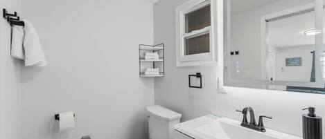 Un baño moderno con inodoro, lavamanos, espejo y toallero.