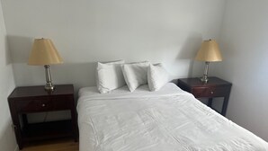 A neatly made bed with white bedding, two bedside tables with lamps, and a wooden floor. - OCEANFRONT PENTHOUSE (Wildwood Crest)