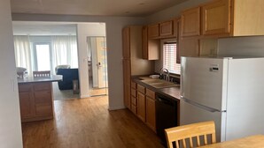 A kitchen with wooden cabinets, a refrigerator, a sink, and a dining area with a table and chairs. - OCEANFRONT PENTHOUSE (Wildwood Crest)