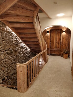 Eine Holztreppe mit einer Steinmauer an der Seite, die zu einem Raum mit Holzvertäfelung und einem kleinen Holzschemel führt.