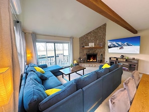 Ein Wohnzimmer mit Kamin aus Stein, einem großen an der Wand befestigten Fernseher und einer Couch mit Kissen.