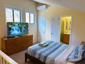 Ein Schlafzimmer mit Bett, Kommode, Fernseher und einer Badezimmertür.