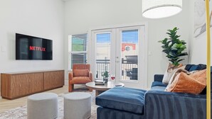 En moderne stue med et fladskærms-tv, en sofa, skærmstole, et sofabord og en potteplante.