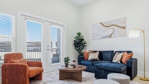 En moderne stue med sofa, lænestol, sofabord, skottomaner og en potteplante.