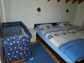 Ein Schlafzimmer mit einem Babybett, einem Bett mit gemusterten Betttextilien und einem Nachttisch.