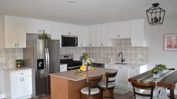 Una cocina moderna con armarios blancos, electrodomésticos de acero inoxidable, una isla central con taburetes y un salpicadero con diseño.