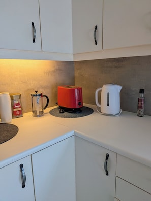 Ett kök med vita skåp, en röd brödrost, en vit vattenkokare, en glaskaraff och en flaska med kryddor.