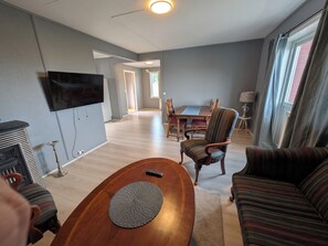 A living room with a TV, a wooden coffee table, a striped sofa, a dining table with chairs, and a lamp.