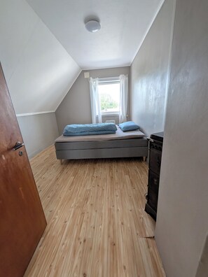 Une petite pièce avec un toit en pente, un lit simple, une fenêtre avec des rideaux et un plancher en bois.