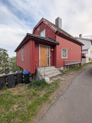 A red house with a wooden door, a small porch, and steps leading to the entrance.
