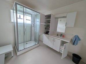 Un baño con cabina de ducha de vidrio, un lavabo con espejo y un pequeño cubo de basura.