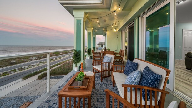 Ein Balkon mit Gartenmöbeln, Lichterketten und Blick auf das Meer.