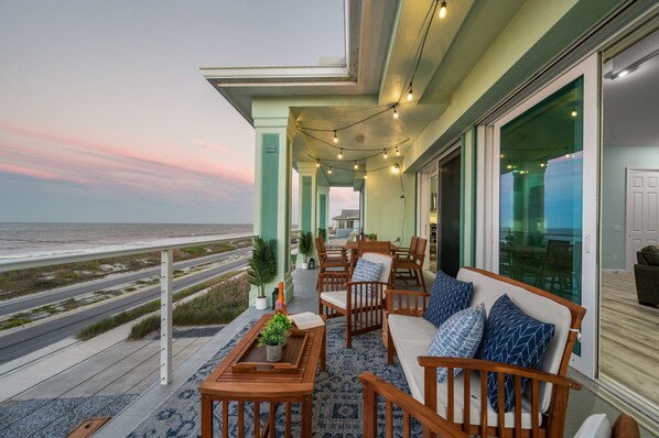 Ein Balkon mit Gartenmöbeln, Lichterketten und Blick auf das Meer.