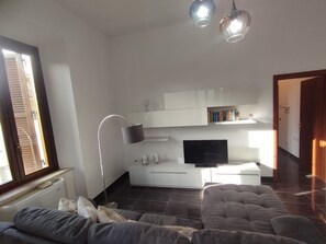 A modern living room with a sofa, a flat-screen TV, a floor lamp, and a bookshelf.