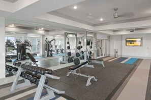 Ein Fitnessraum mit Krafttrainingsgeräten, Spiegeln und einem Fernseher an der Wand.