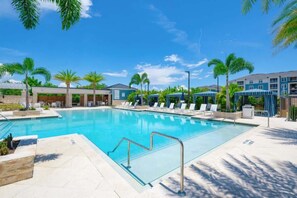 Ein Swimmingpool mit klarem, blauem Wasser, umgeben von Liegestühlen und Palmen.