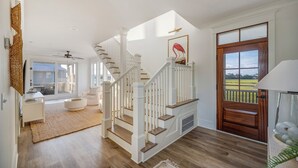 A spacious living area with a staircase, a wooden door, and a view of the outdoors. - Private pool, putting green, kayaks, beautiful sunsets, ocean & marsh views! (Fripp Island)