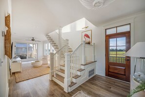 A spacious living area with a staircase, a wooden door, and a view of the outdoors. - Private pool, putting green, kayaks, beautiful sunsets, ocean & marsh views! (Fripp Island)
