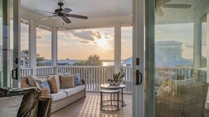 A covered outdoor area with a sofa, a small table, and a wicker chair. - Private pool, putting green, kayaks, beautiful sunsets, ocean & marsh views! (Fripp Island)