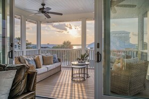 A covered outdoor area with a sofa, a small table, and a wicker chair. - Private pool, putting green, kayaks, beautiful sunsets, ocean & marsh views! (Fripp Island)