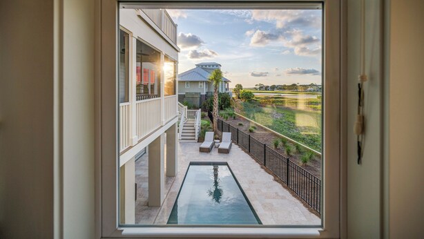 A view from a balcony with a pool, outdoor furniture, and a distant building. - Private pool, putting green, kayaks, beautiful sunsets, ocean & marsh views! (Fripp Island)