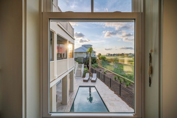 A view from a balcony with a pool, outdoor furniture, and a distant building. - Private pool, putting green, kayaks, beautiful sunsets, ocean & marsh views! (Fripp Island)