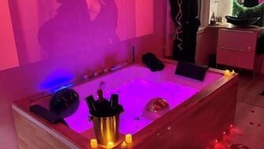 Una habitación con una bañera de madera, velas y una pantalla de proyección con el texto 'ORGVSM'.