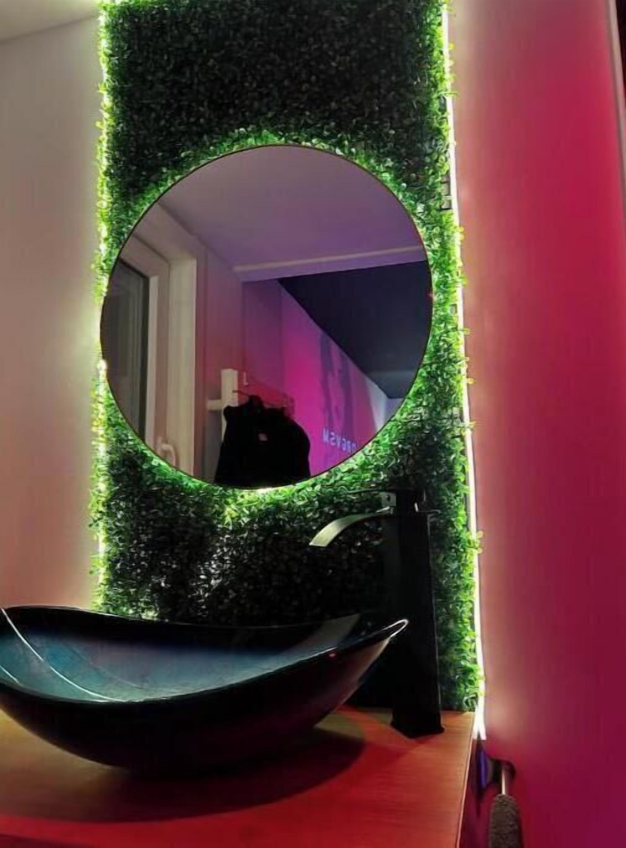 A bathroom with a round mirror, green artificial grass, and a black basin.