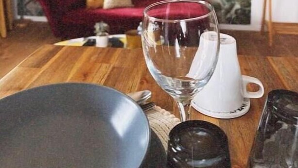 Un comedor con una mesa de madera, un sofá rojo y un mural en la pared con follaje tropical.