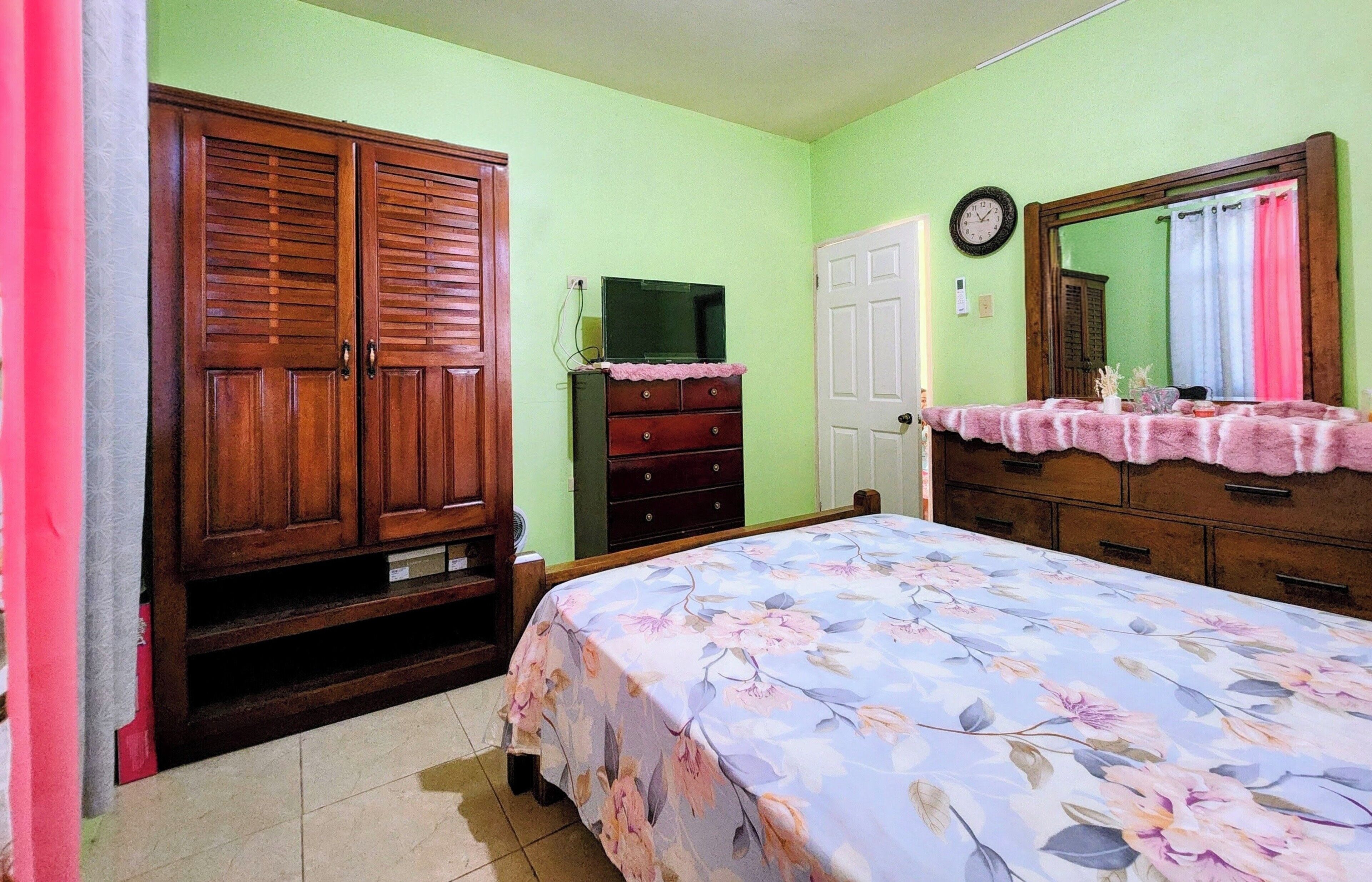 A bedroom with a bed, a dresser, a wardrobe, and a mirror.