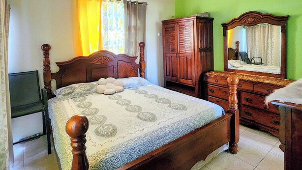 A bedroom with a wooden bed, a wardrobe, a mirror, and a television.