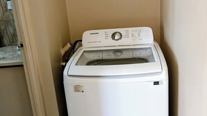 A Samsung front-loading washer in a corner of a room with a tiled floor and a door.