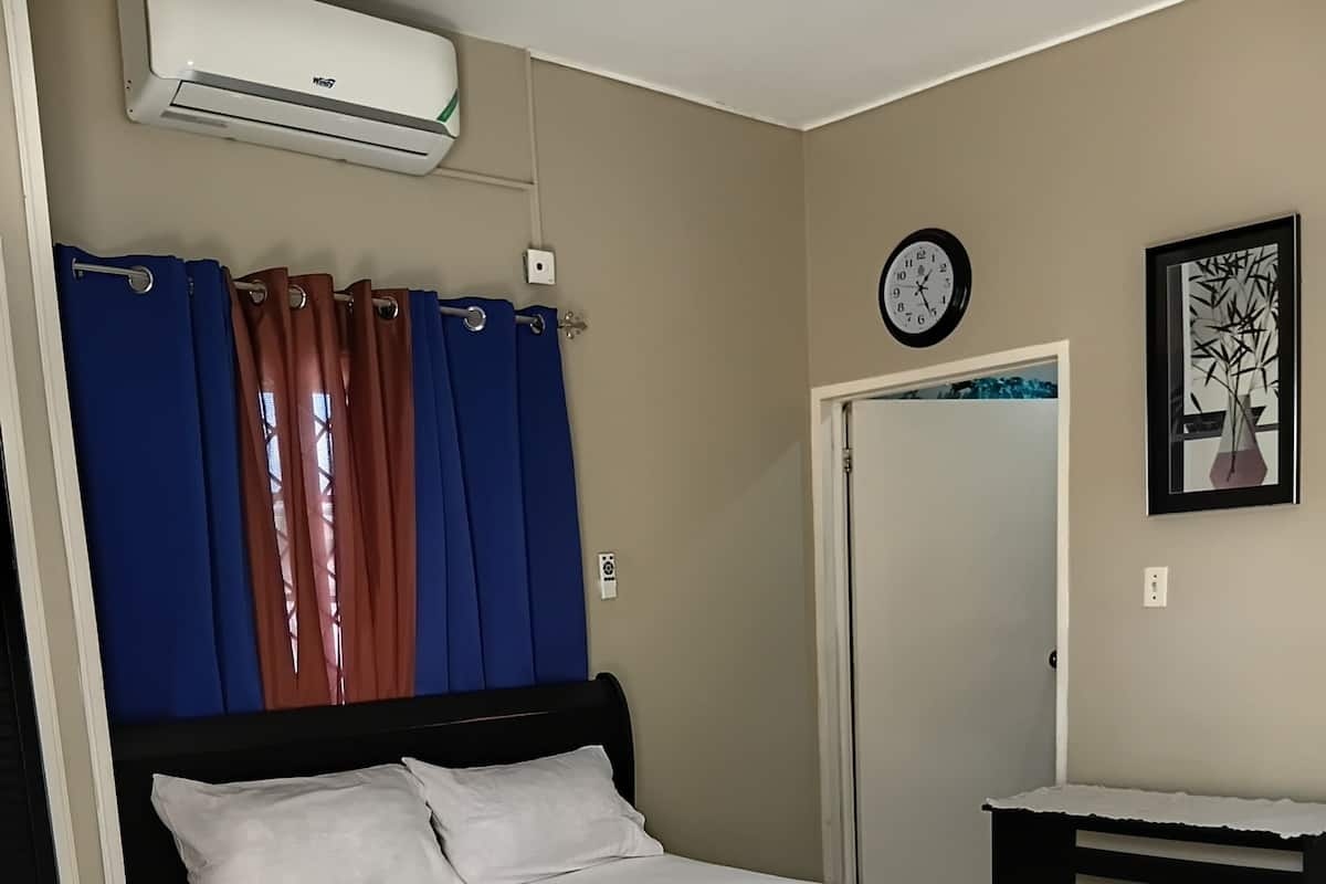 Une chambre à coucher avec un lit, des rideaux, un climatiseur, une horloge et un tableau encadré au mur.